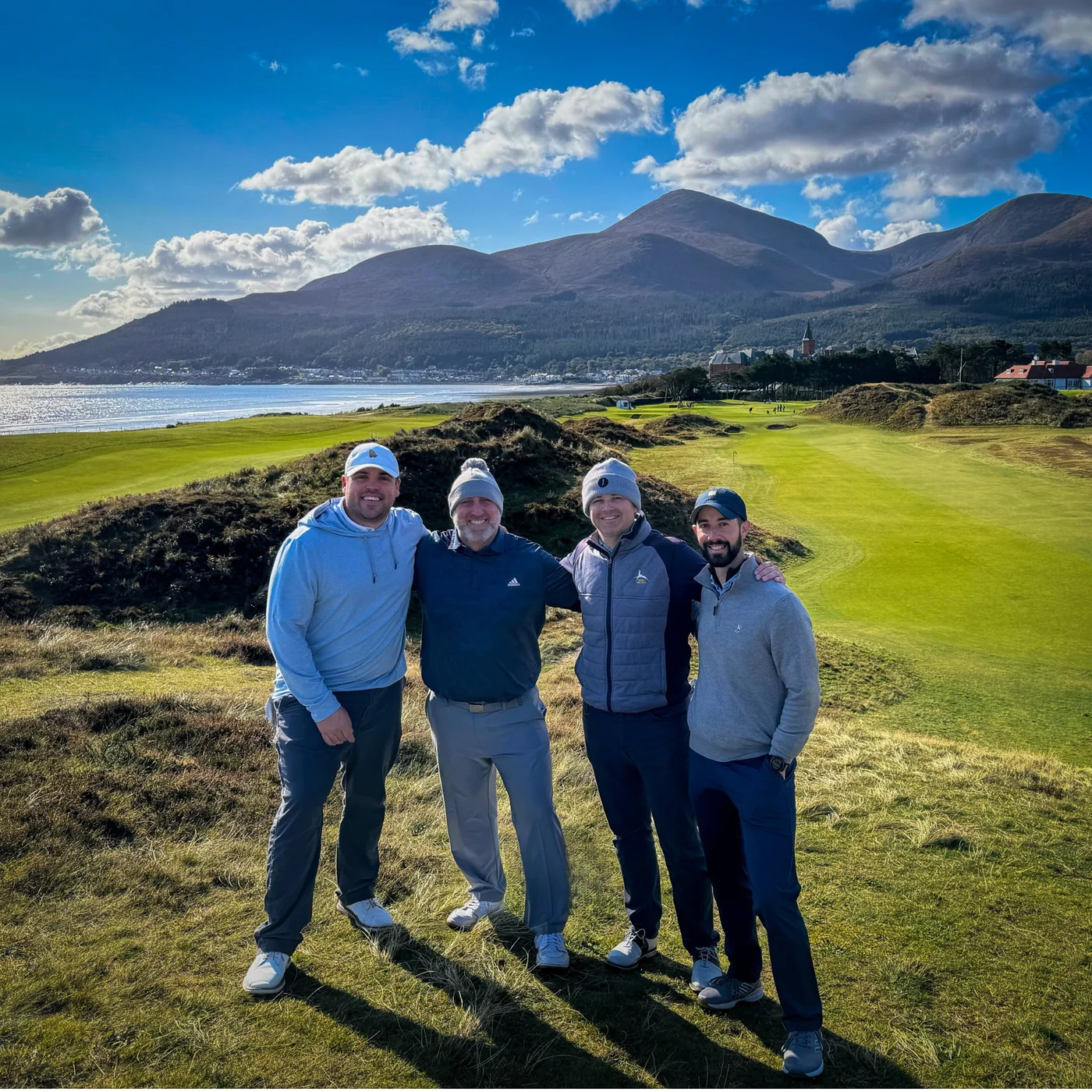 Four golfers smiling together on an Irish links course with the Mourne Mountains behind them